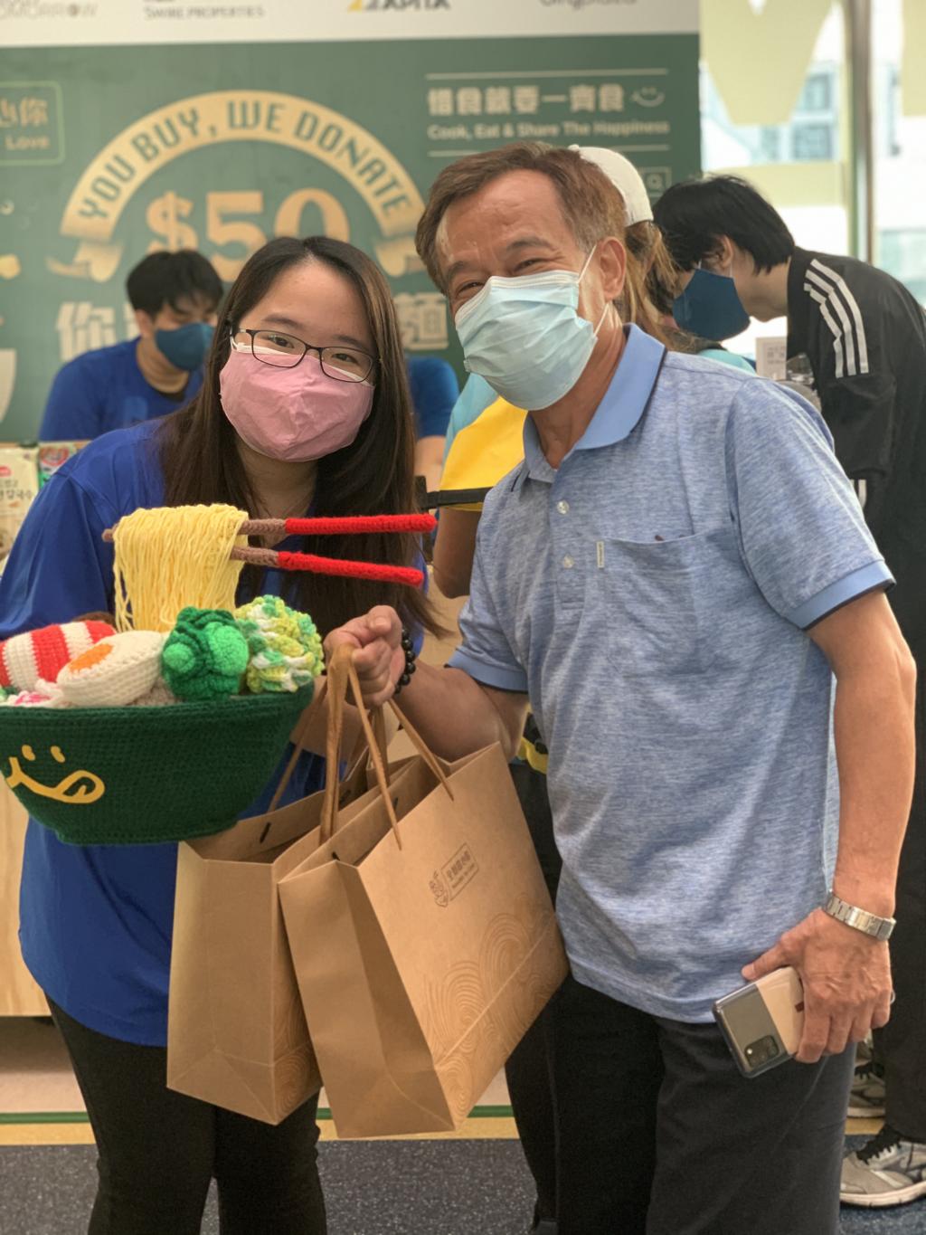 一名青年拿著「全麵關心你」的公仔與顧客合照