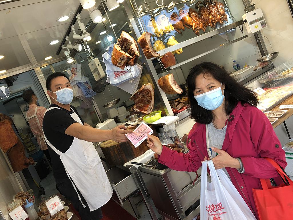 一位女士手持食物券到青衣區內的燒味舖換領一盒燒味飯。
