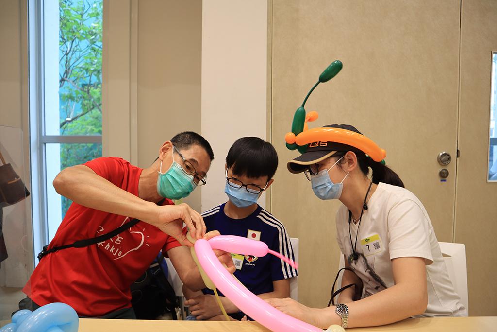 一名馬會義工向男童展示如何扭氣球。