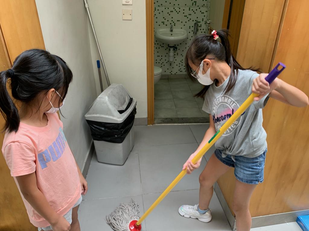 女孩手持地拖清潔廁所外的地板。