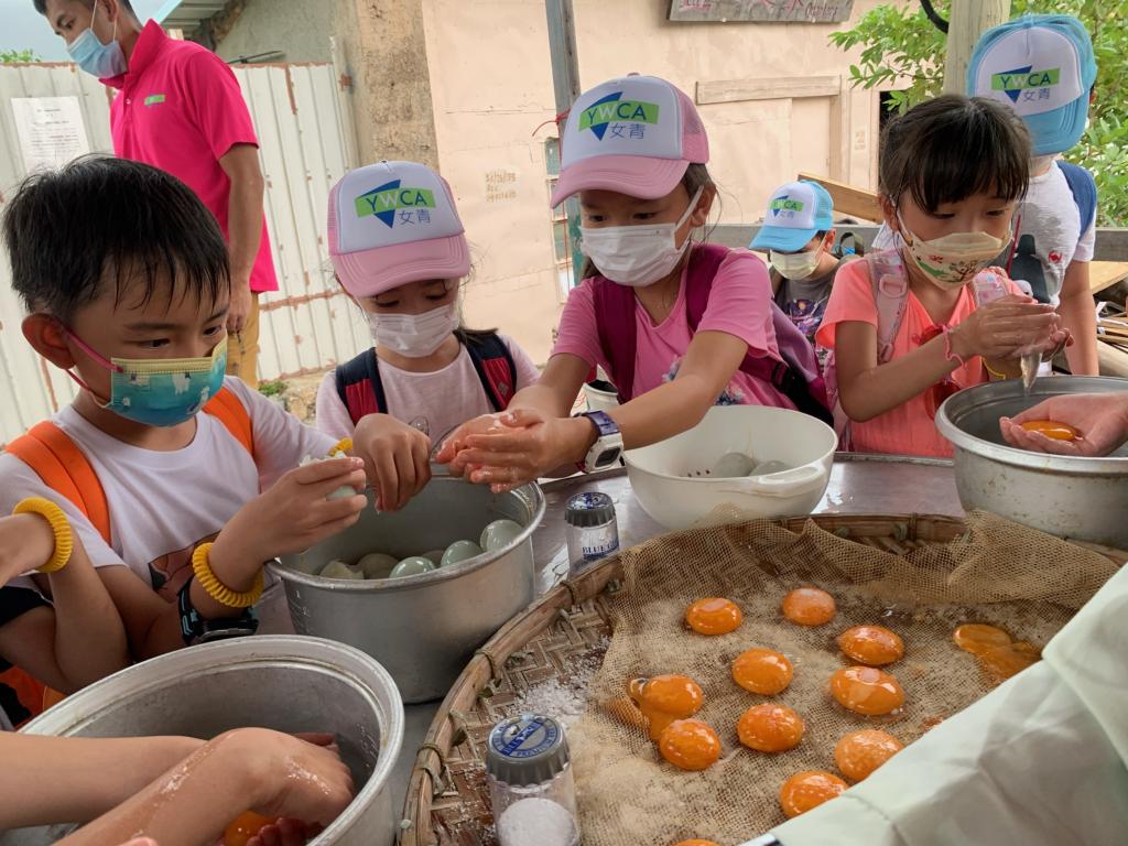 一個男孩及三名女孩小心翼翼地將鴨蛋蛋黃取出並放置在佈滿鹽的竹網篩上。
