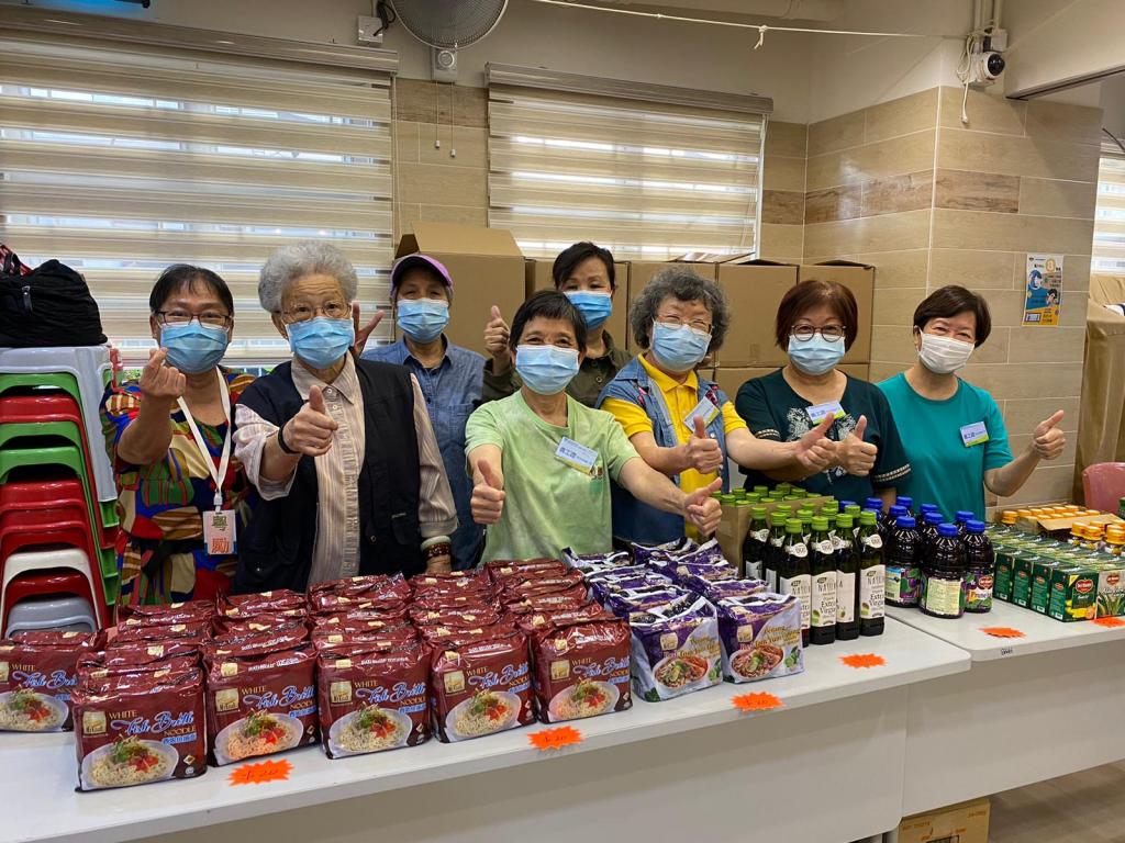 八名長者站在擺放了貨品的長桌後方讚好