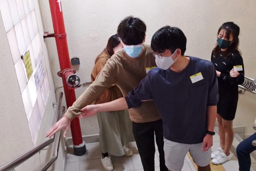 一名青年以領路法引領另一名蒙眼青年走上樓梯