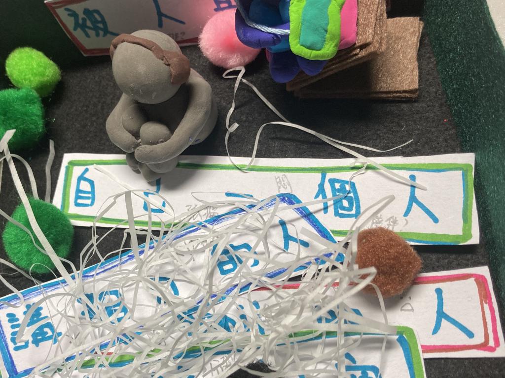 An art piece with clay, chopped paper, and paper with text.