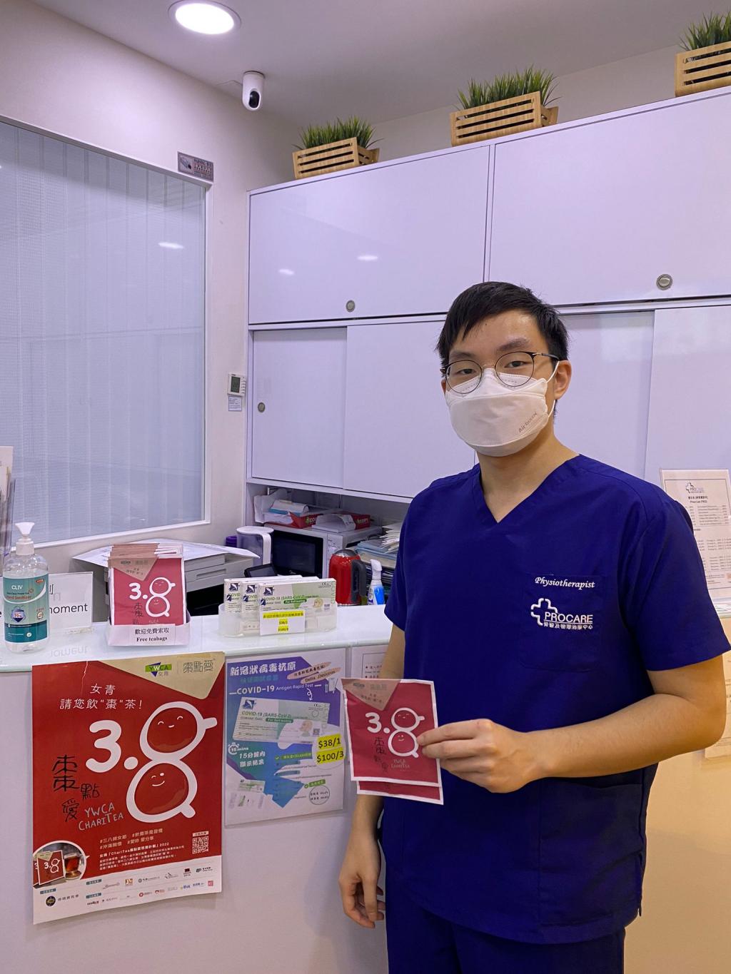 A physiotherapist stands in front of a counter in a clinic, with two tea bags in his hands.