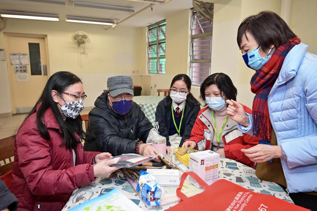 Four ladies help an old man to take out the thermal underwear, scarves, wool socks, etc. from a bag.